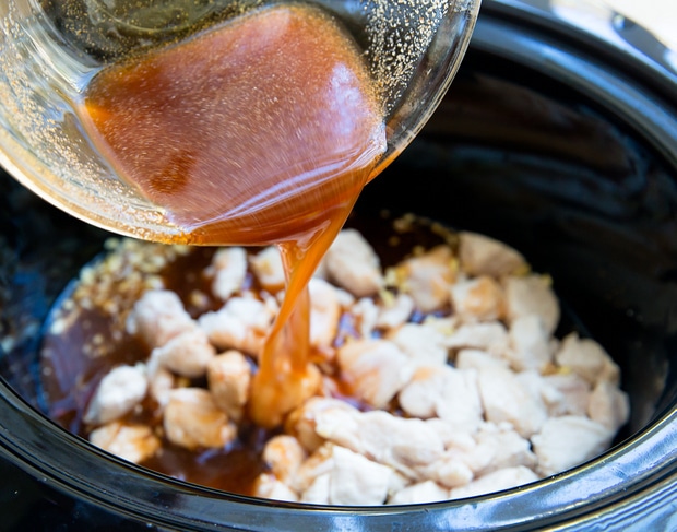 photo showing honey garlic sauce being poured over chicken in a slow cooker