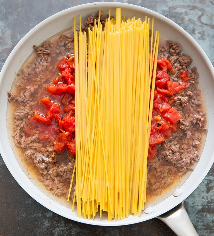 step by step photo showing the spaghetti being added to the beef and tomatoes