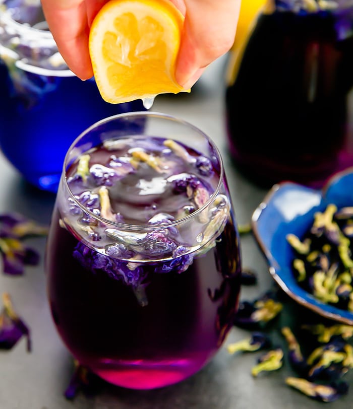 a photo of lemon being squeezed into a glass of butterfly pea flower tea lemonade