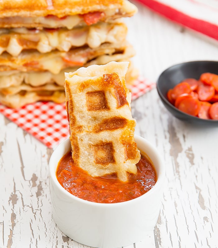 part of a Waffled Pepperoni Pizza Grilled Cheese dipped in marinara