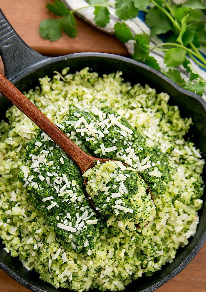 overhead shot of pesto cauliflower rice in a skillet with a wooden spoon