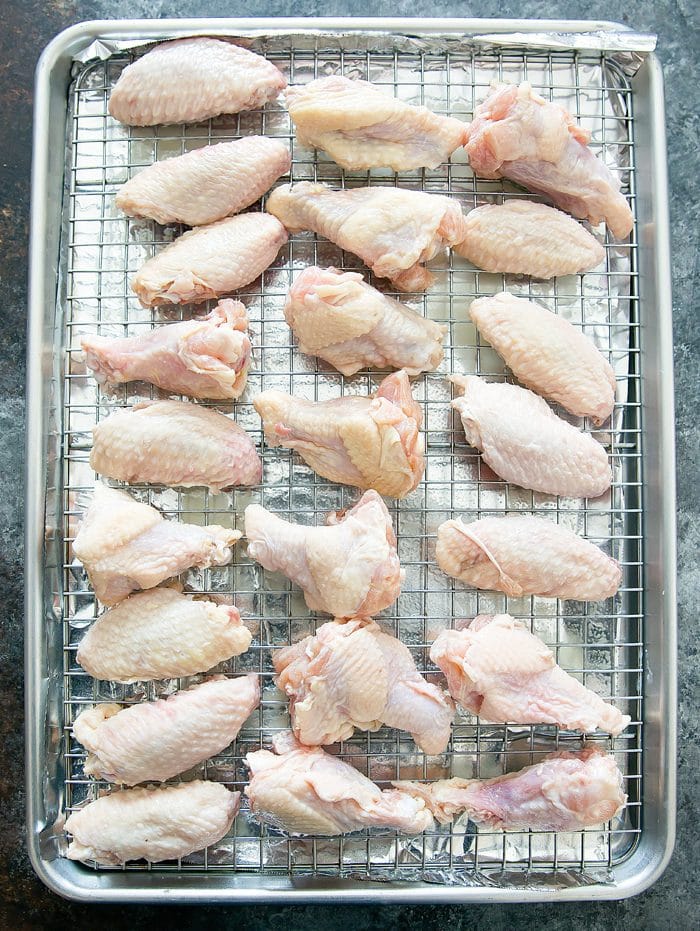raw chicken wings on a wire baking rack placed on a sheet pan lined with tin foil