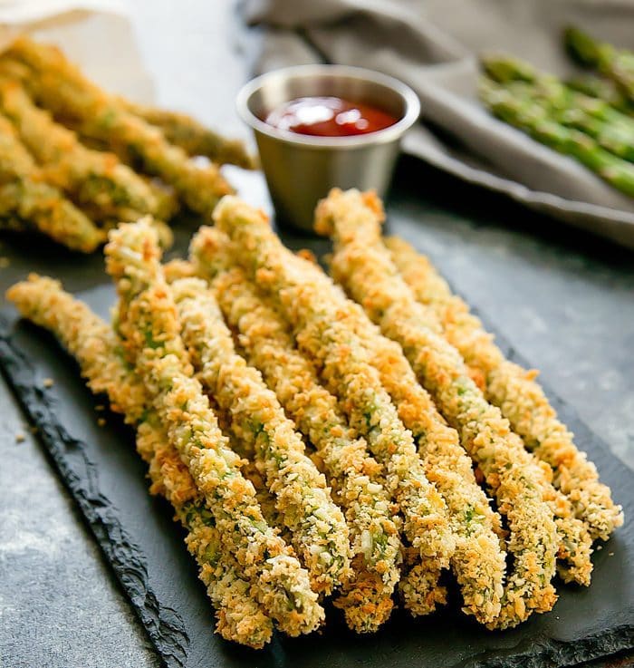 baked parmesan asparagus fries on a slate board with a dipping sauce in the background