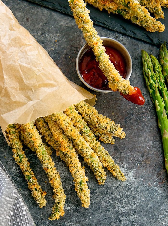 overhead shot of baked parmesan asparagus fries with one fry on top of the dipping sauce bowl