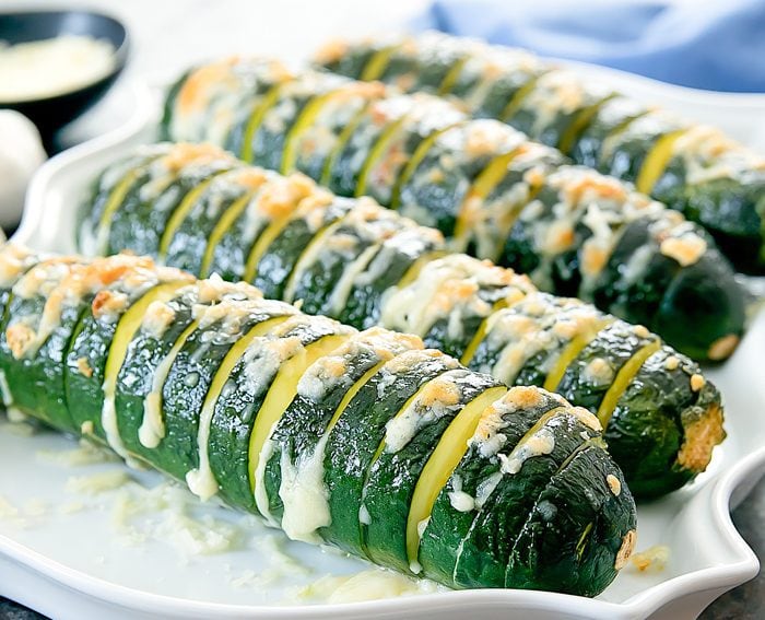 close-up of four garlic parmesan hasselback zucchinis lined up on a plate