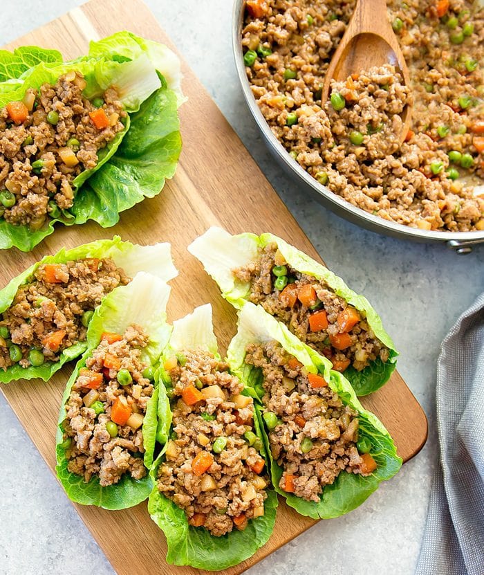 overhead shot of five chinese lettuce wraps on a cutting board with a skillet filled with more filling on the side