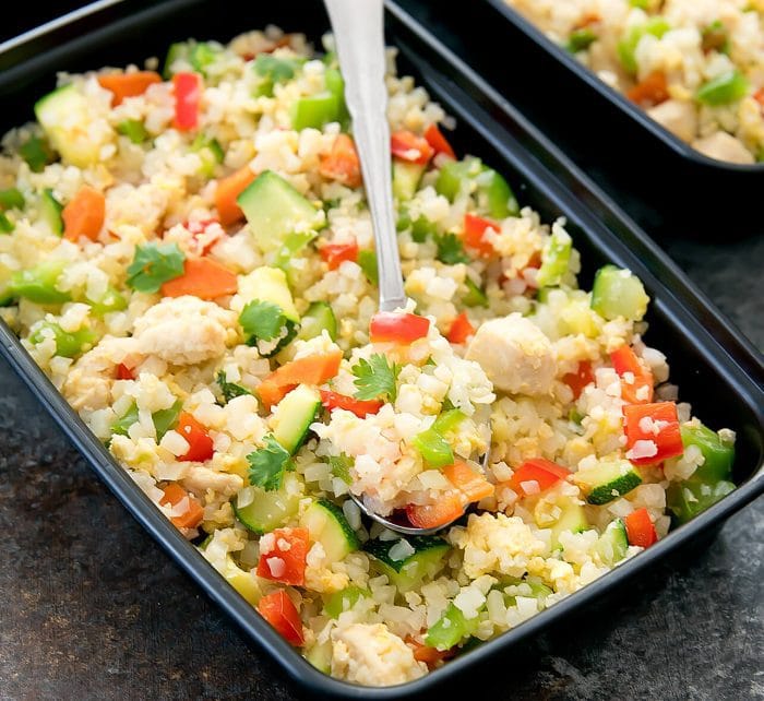 a close-up photo of chicken cauliflower fried rice in a container with a spoon