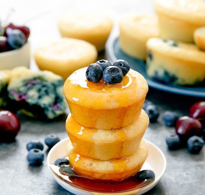 a stack of three buttermilk pancake muffins topped with fresh blueberries and maple syrup