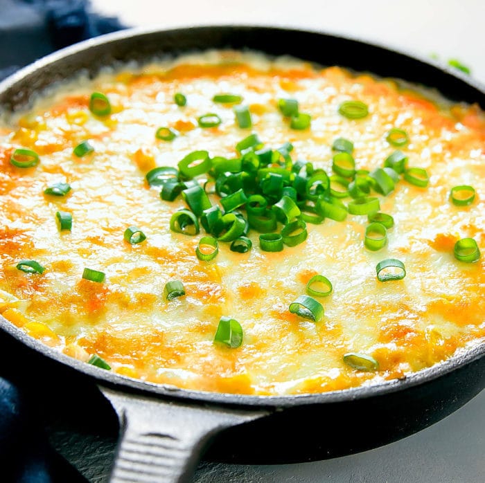 a skillet of Korean corn cheese garnished with sliced scallions