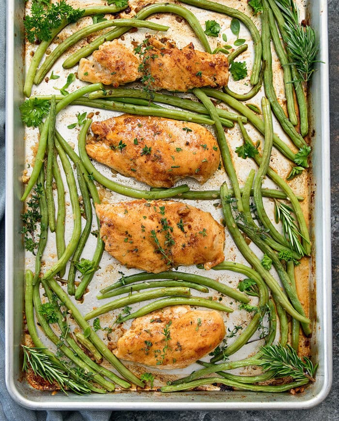 Cooked chicken breasts on a sheet pan with green beans