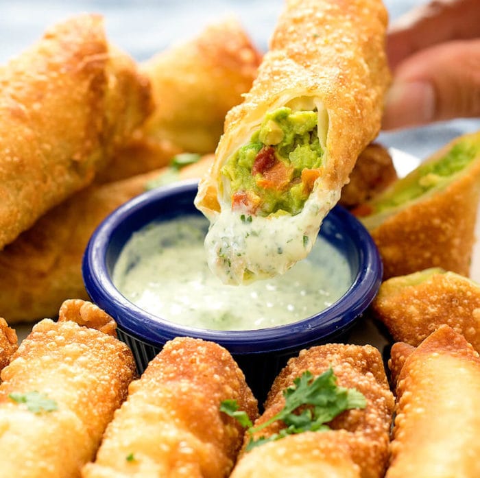 Close-up of avocado egg roll being dipped in cilantro ranch dressing