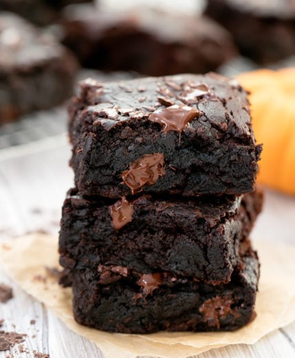 stack of 3 pumpkin brownies with brownies resting on cooling rack in background