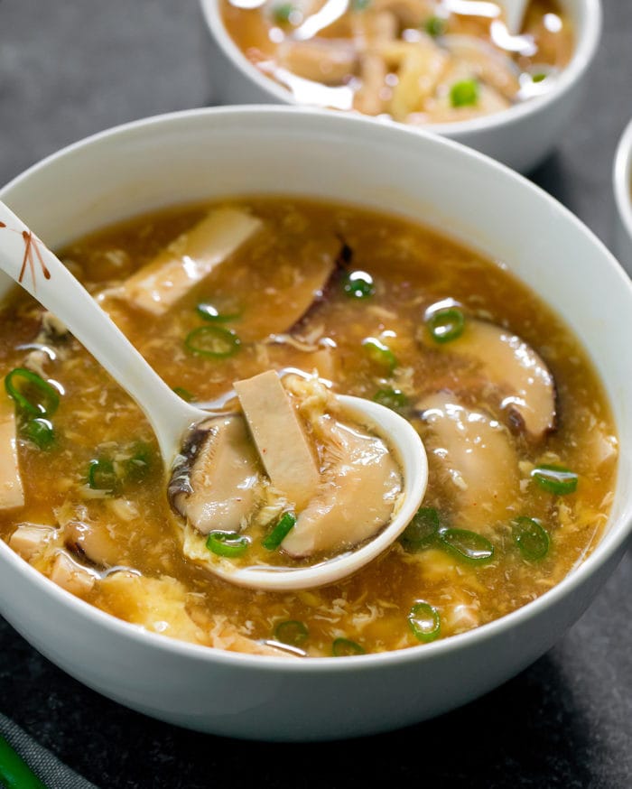 close-up photo of a spoon dipping into a bowl of hot and sour soup