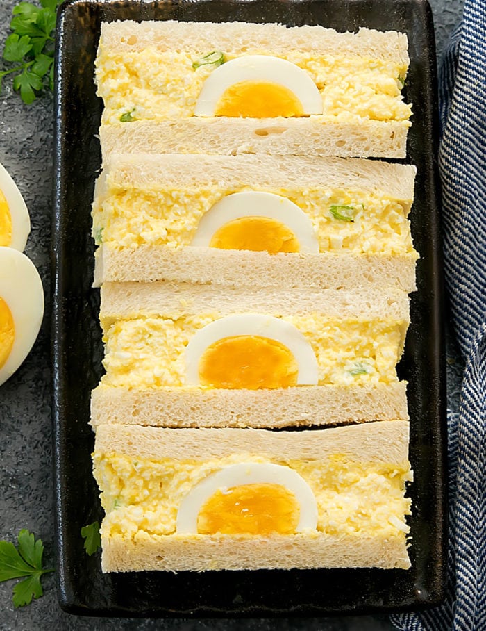 overhead photo of Japanese egg salad sandwiches sliced in half with a soft boiled egg in the center