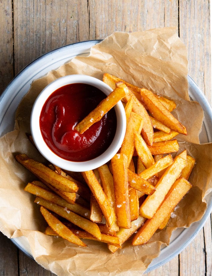 overhead photo of a plate of fries with one being dipped in ketchup