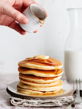 syrup being poured on a stack of pancakes