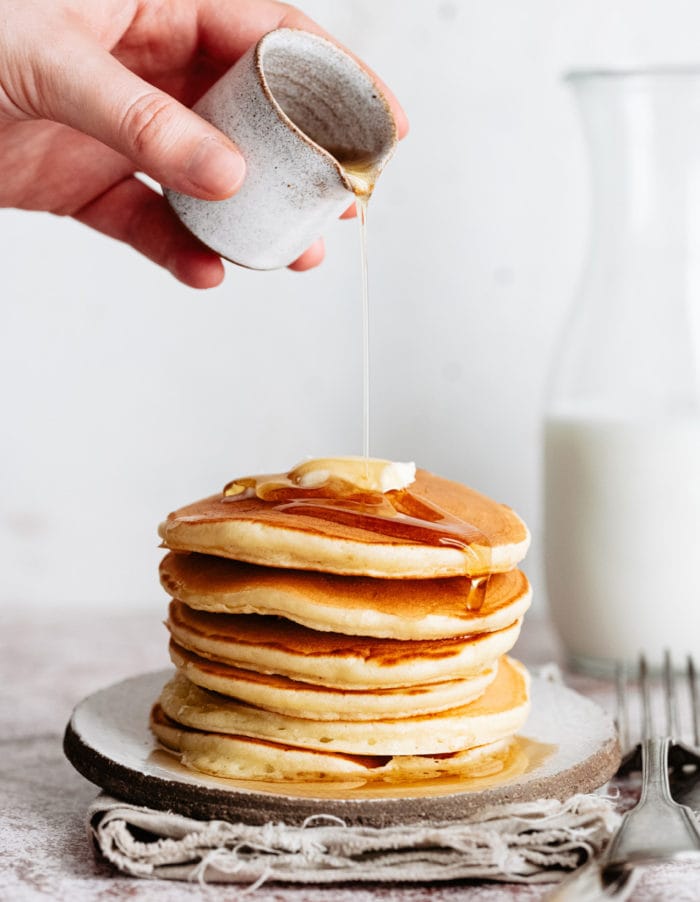 syrup being poured on a stack of pancakes