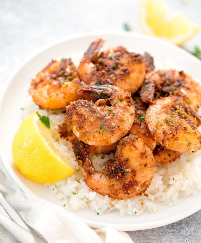 garlic shrimp on a plate with rice and a lemon wedge.