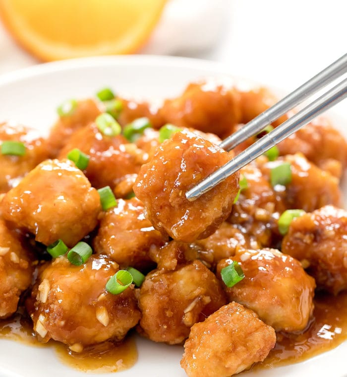 a plate of orange chicken with a piece picked up by chopsticks.