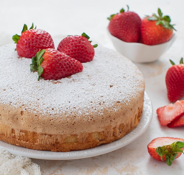 a cake dusted with powdered sugar and topped with fresh strawberries.