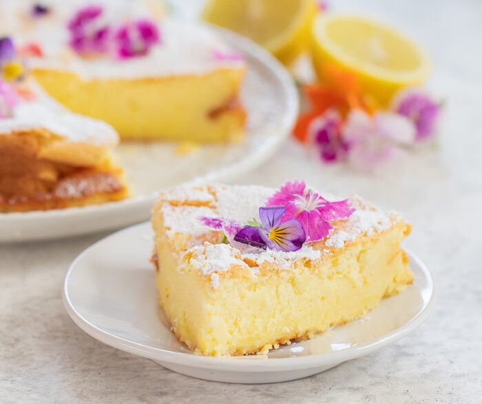 a slice of lemon cake topped with edible flowers on a plate.