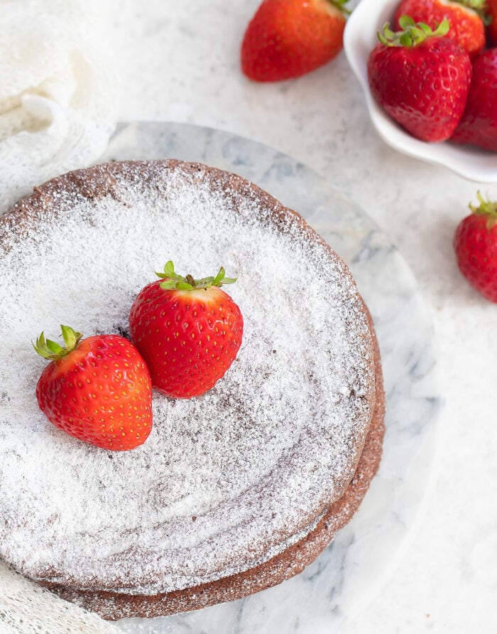 a chocolate cake dusted with powdered sugar and topped with two strawberries.
