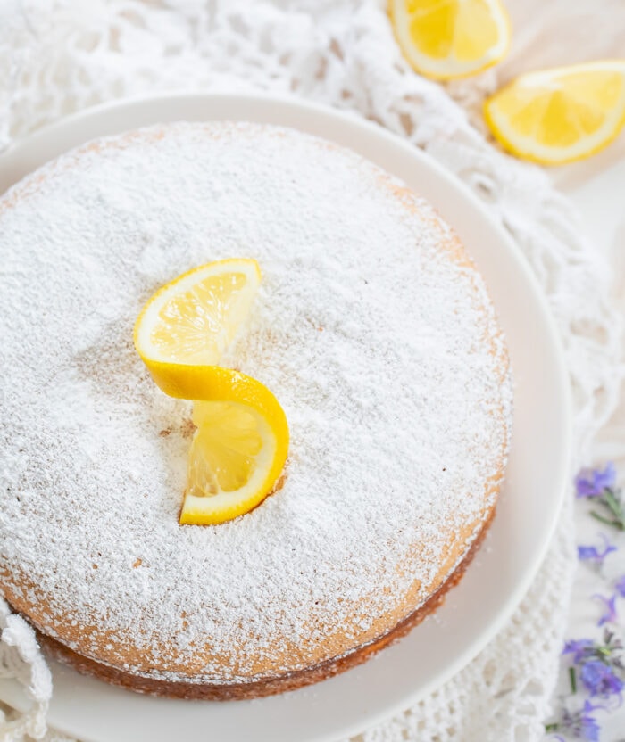 a whole lemon cake dusted with sugar with a lemon garnish.