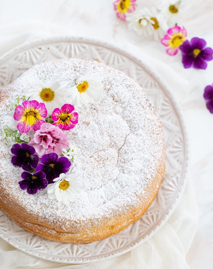 a sponge cake dusted with powdered sugar and decorated with flowers.