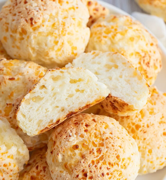 a roll split in half on top of a pile of cheese rolls.