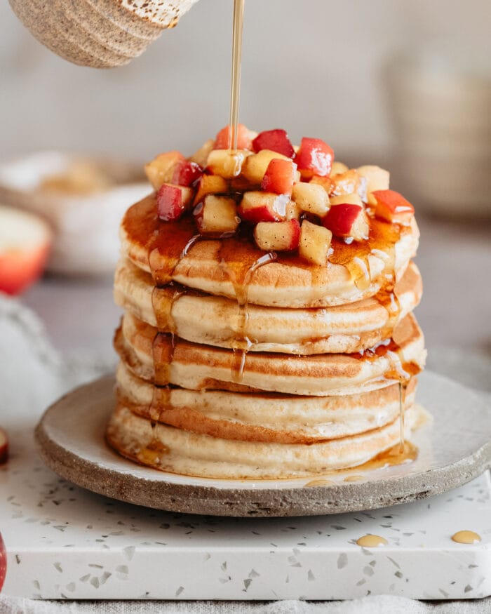 syrup being poured over a stack of apple pancakes.