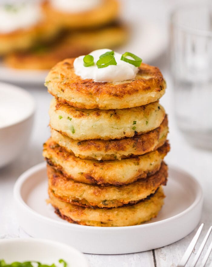 fritters stacked on a plate and topped with sour cream and sliced scallions.