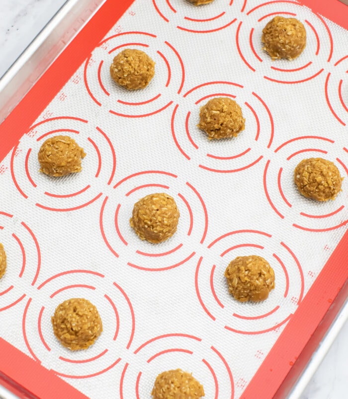 cookies dough balls on a cookie sheet lined with a baking mat.
