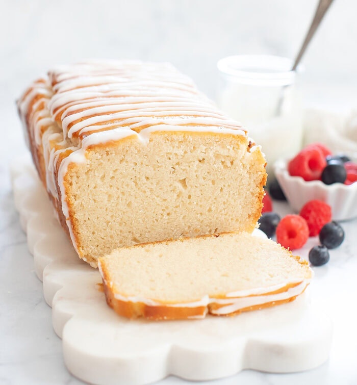 French yogurt cake on a white scalloped cutting board with a slice cut from it