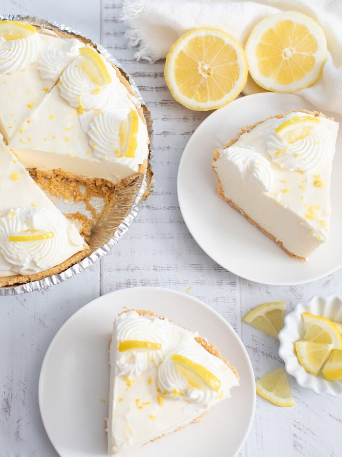 A lemon cream pie with a slice cut from it and to slices on plates