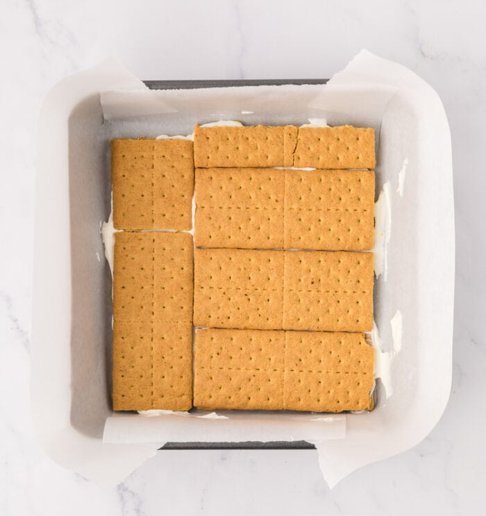 An 8 x 8 inch baking pan with whipped cream and graham crackers