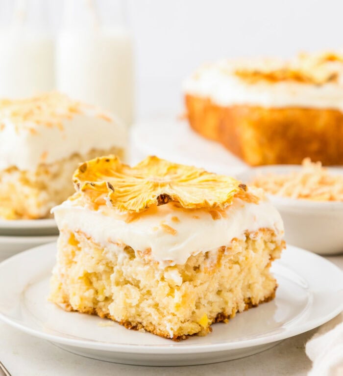 Close up of a slice of pineapple cake topped with cream cheese frosting, toasted coconut shreds and dried pineapple slices