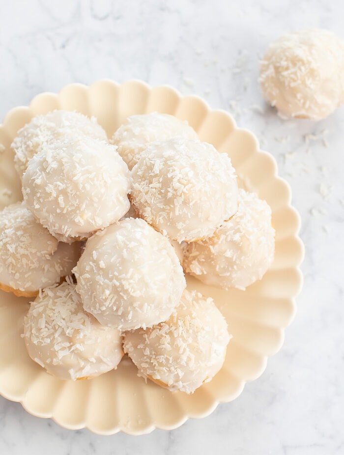 A pile of coconut donuts with a glaze and shredded coconut on top