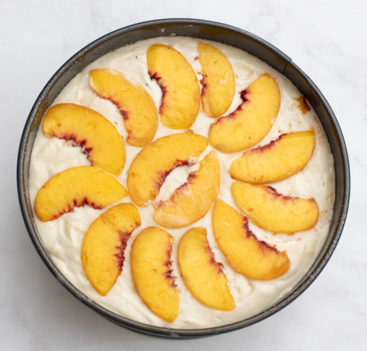 Cake batter in a cake pan topped with peach slices
