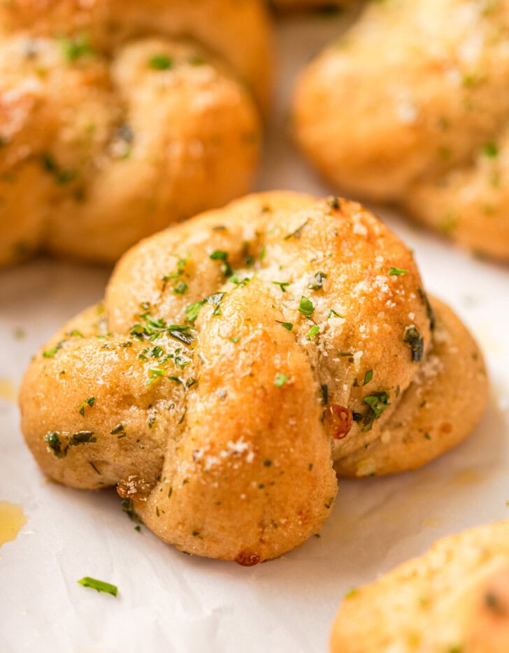 A garlic knot garnished with grated parmesan cheese and finely chopped parsley