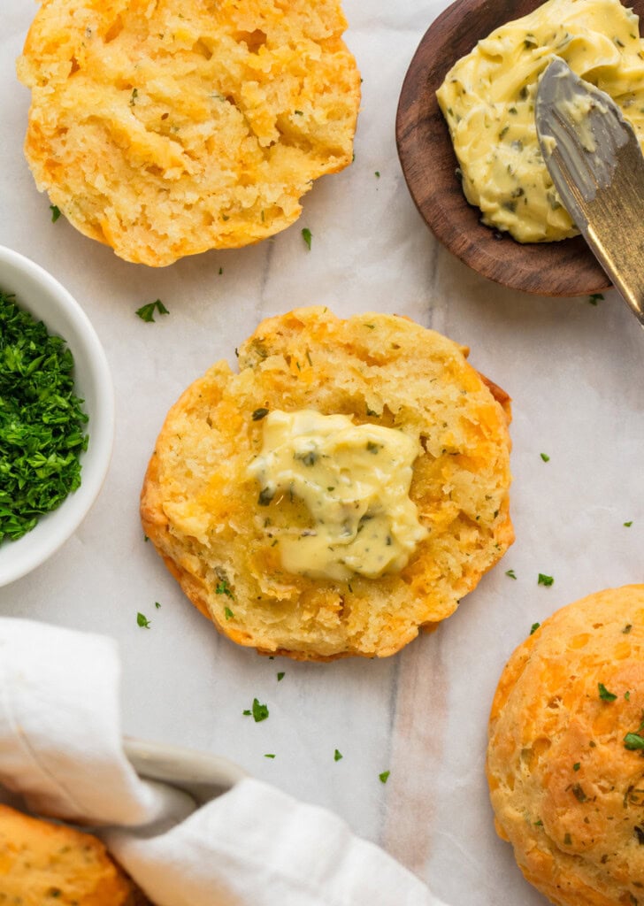 A biscuit cut in half with herbed butter spread on one half