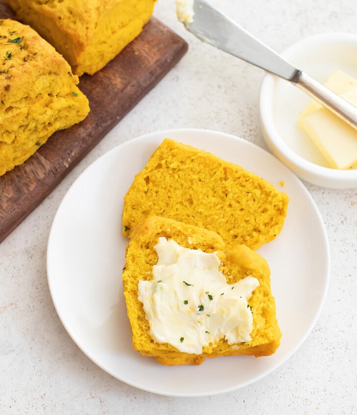A pumpkin biscuit cut in half with butter spread on one half