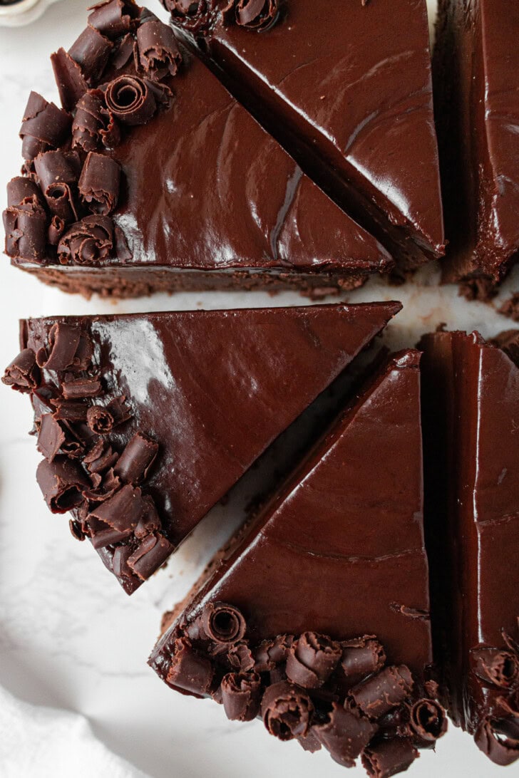A chocolate cake cut into slices with chocolate frosting and chocolate curls