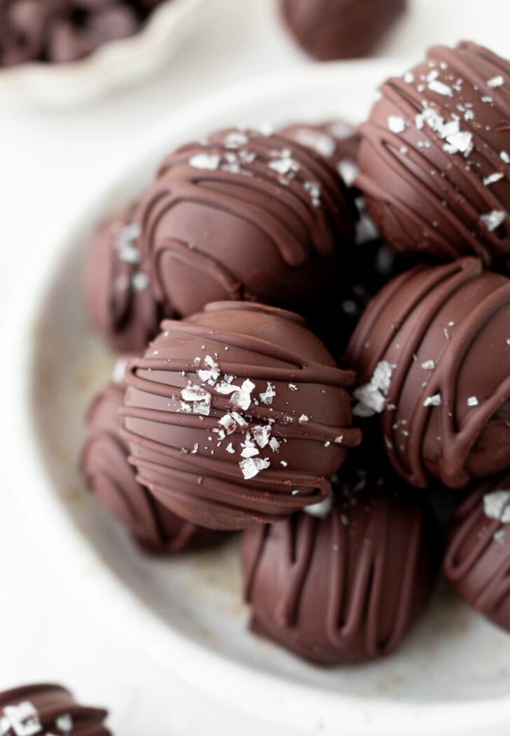 Close-up of chocolate-coated no-bake brownie balls drizzled with chocolate and topped with flaky salt on a plate