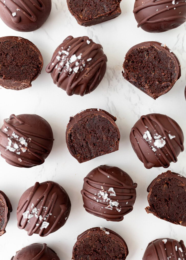 Chocolate-coated no-bake brownie balls with chocolate drizzle and flaky salt, some cut open to show the fudgy center.