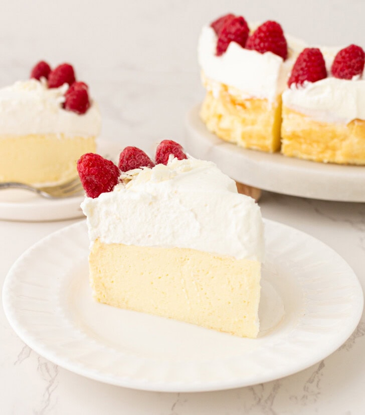 A slice of Yogurt Cheesecake on a plate with whipped cream frosting and fresh raspberries on top