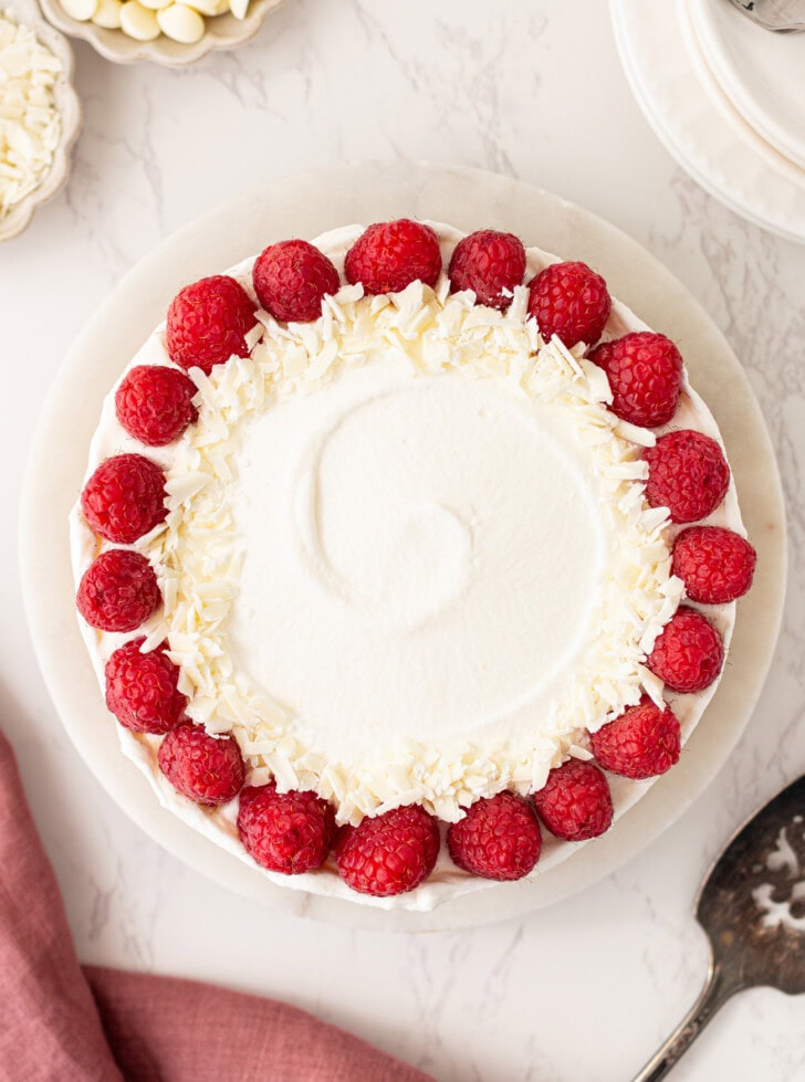 A decorated Yogurt Cheesecake with whipped cream frosting and fresh raspberries