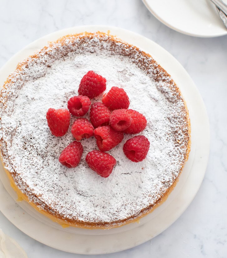 A cheesecake dusted with powdered sugar and fresh raspberries