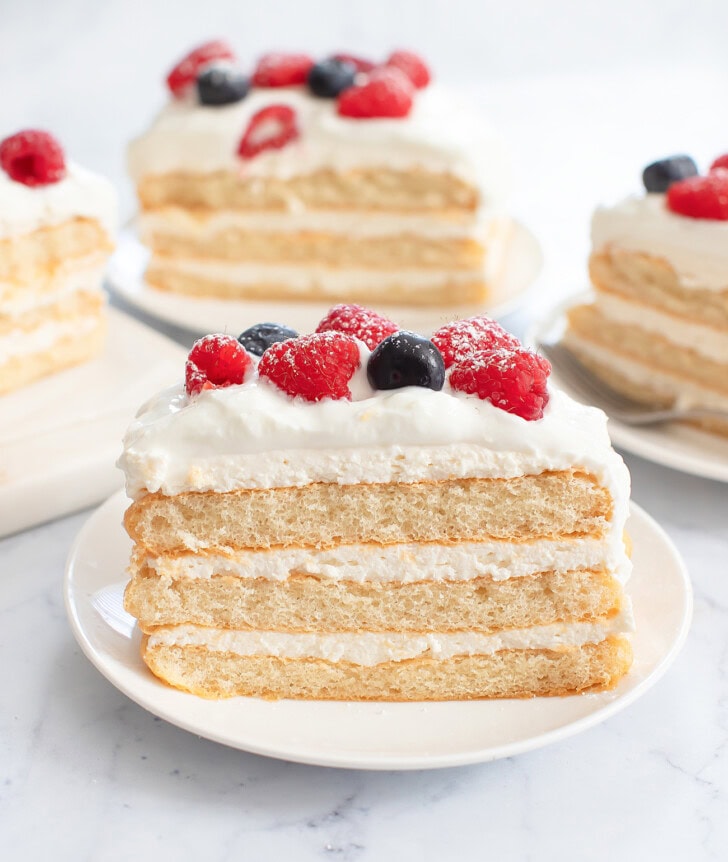 A slice of cake with whipped cream frosting and fresh berries on top