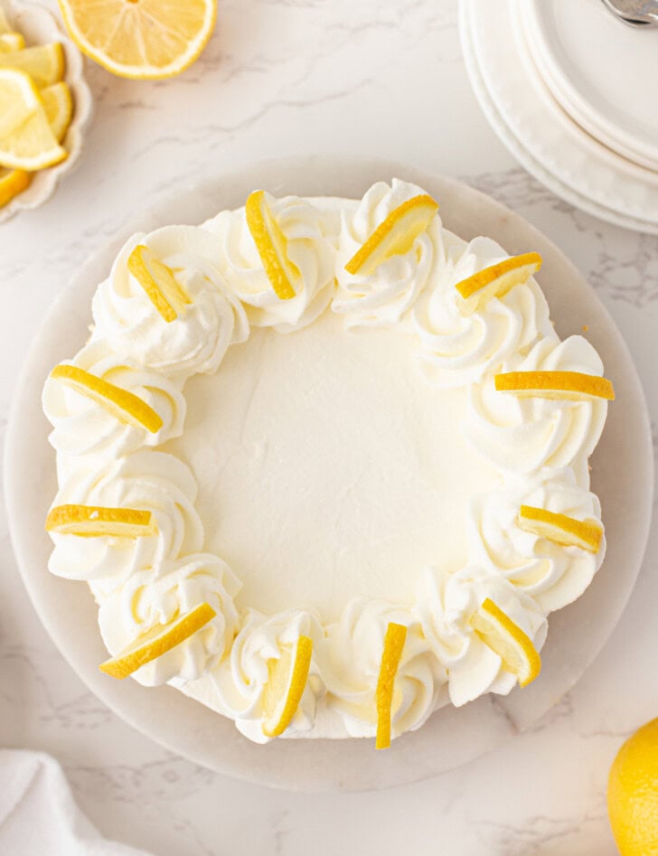 A Lemon Yogurt Cheesecake with whipped cream frosting and lemon slices on top