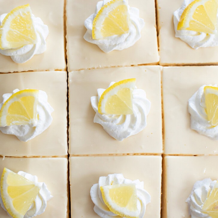 Lemon Cheesecake Bars garnished with whipped cream and lemon wedges